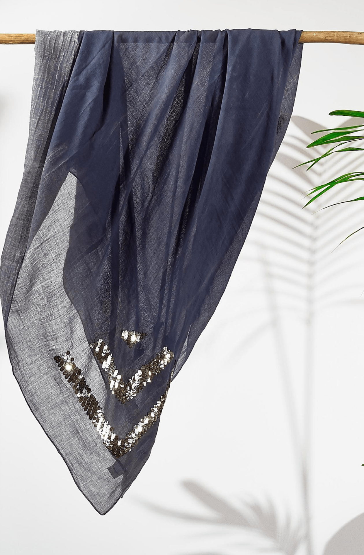 Grey cotton scarf with sequin details draped over a wooden rod on a white background.
