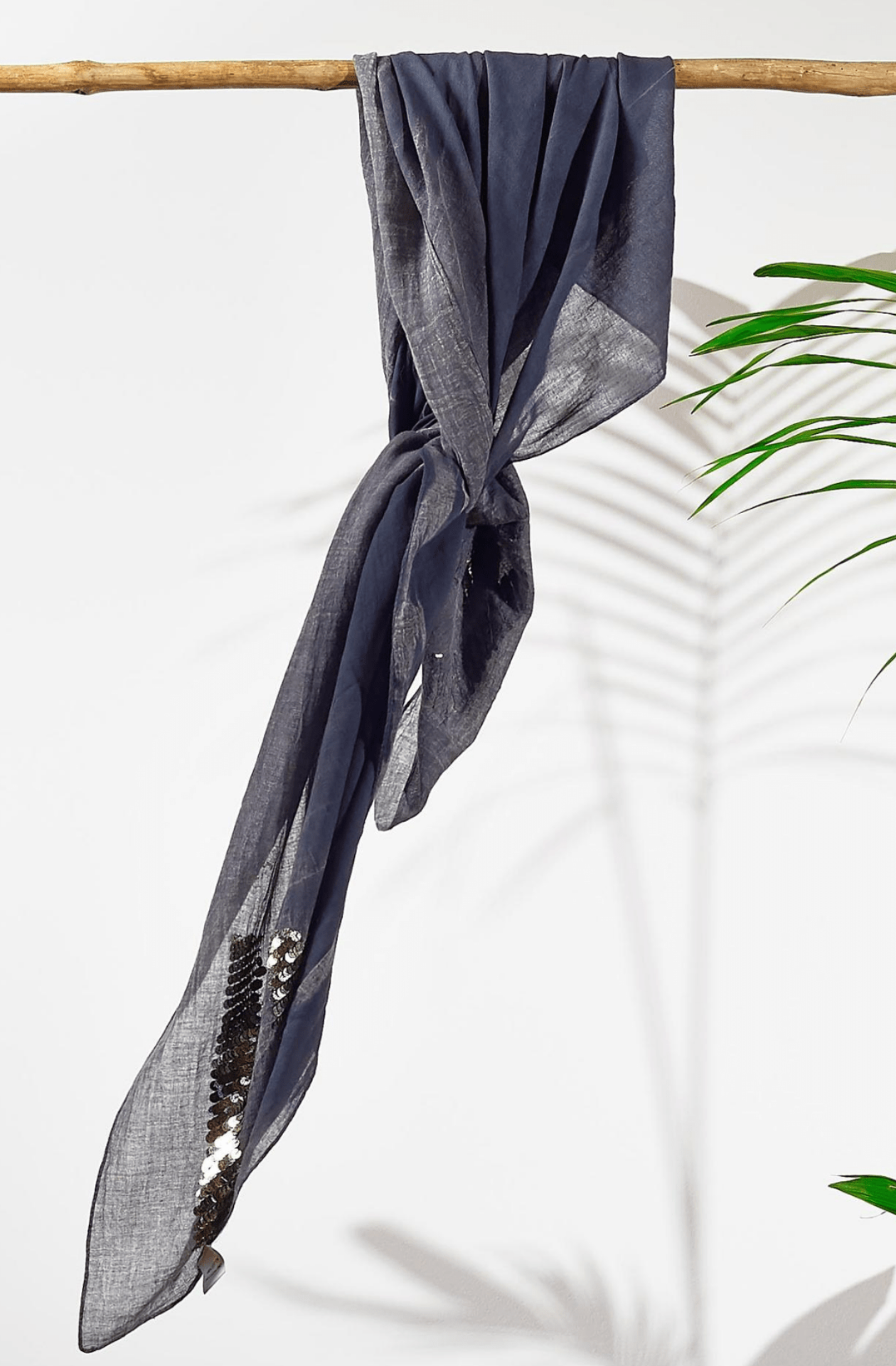 Grey square cotton scarf with sequin details draped over a wooden rod on a white background.