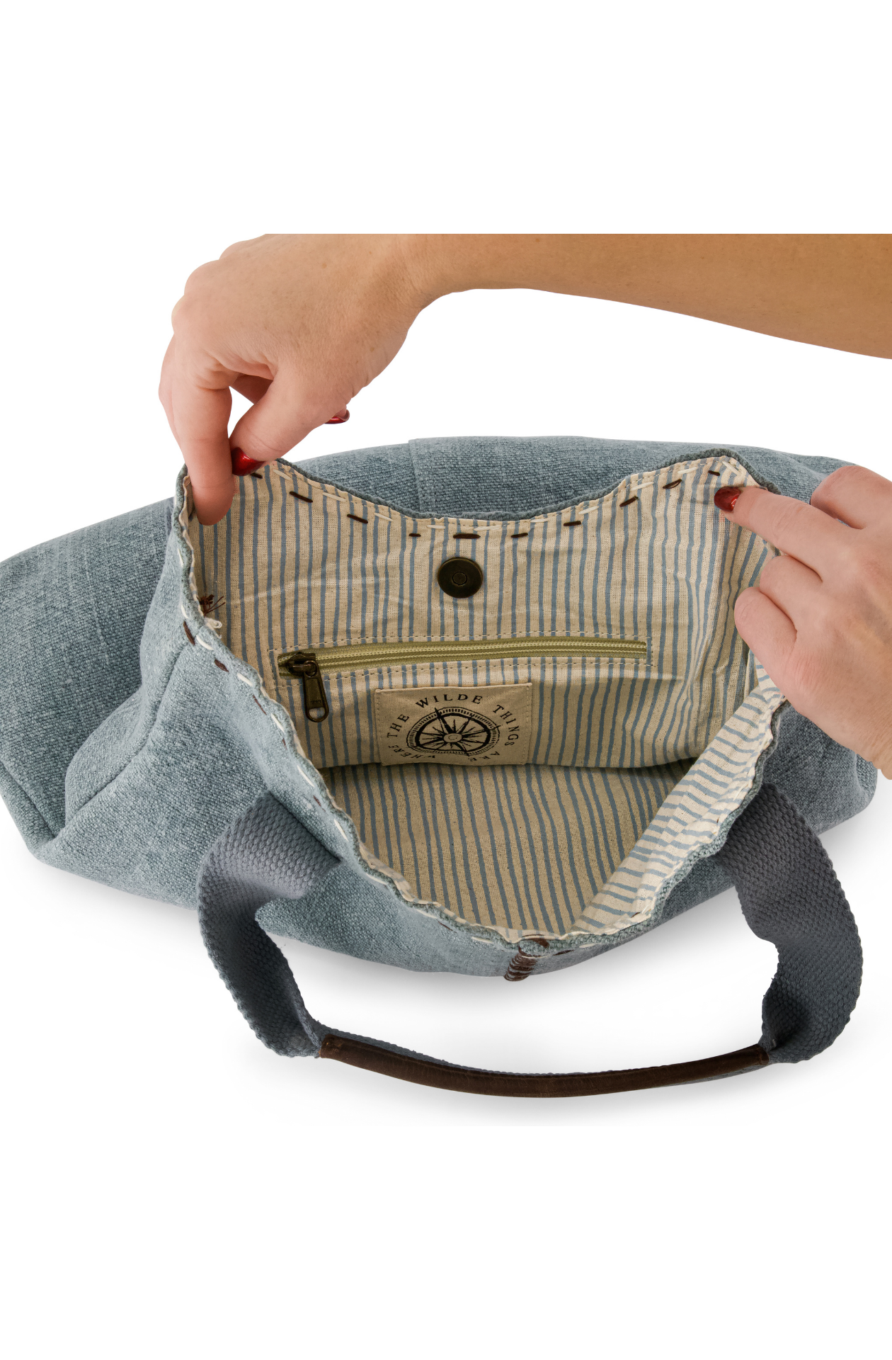 Light blue, chambray coloured jute bag showing pin striped cotton lining and interal zip pocket, hold open by a model's hands.