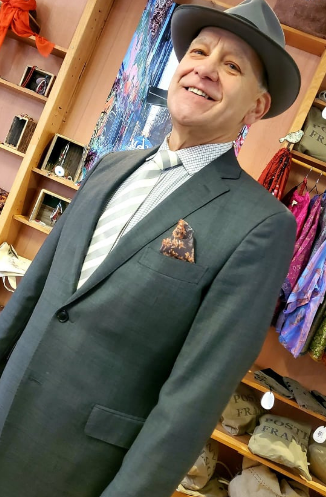 A portrait of a man with a deep grey suit on, a brown and orange pocket square in his breast pocket