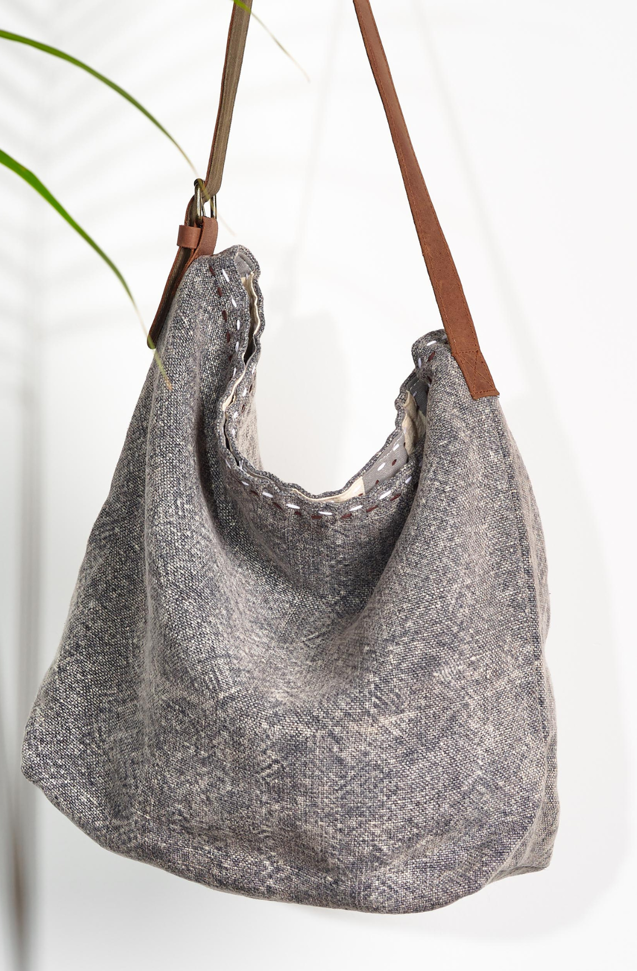 Smoke All the world Jute Bag. The washed light grey is contrasted with two lines of black and white stitching at the top of the bag in between the warm brown leather strap with a golden buckle.