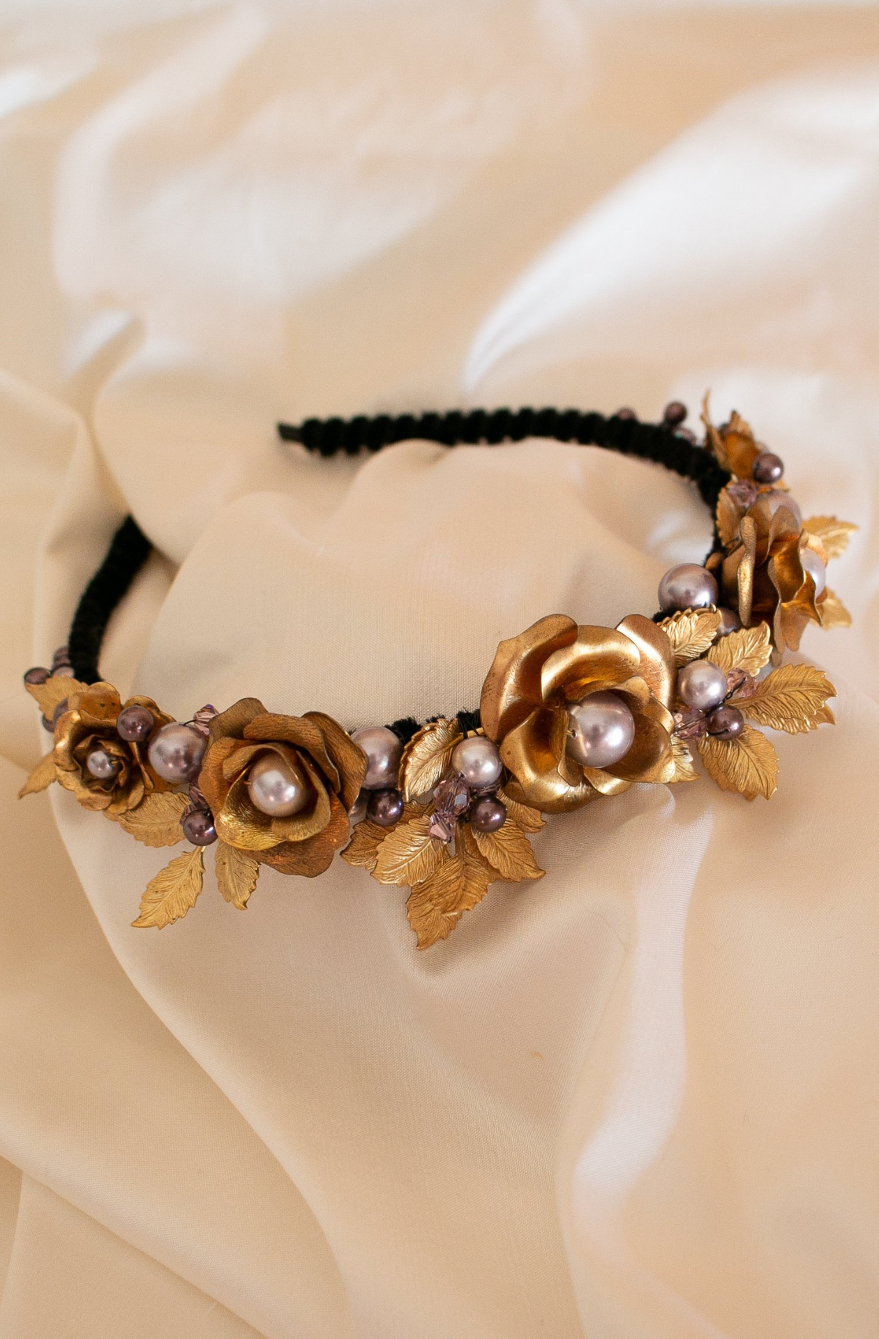 A narrow black velvet covered headband featuring vintage golden brass roses and leaves amongst mixed shades of lavender Swarovski pearls