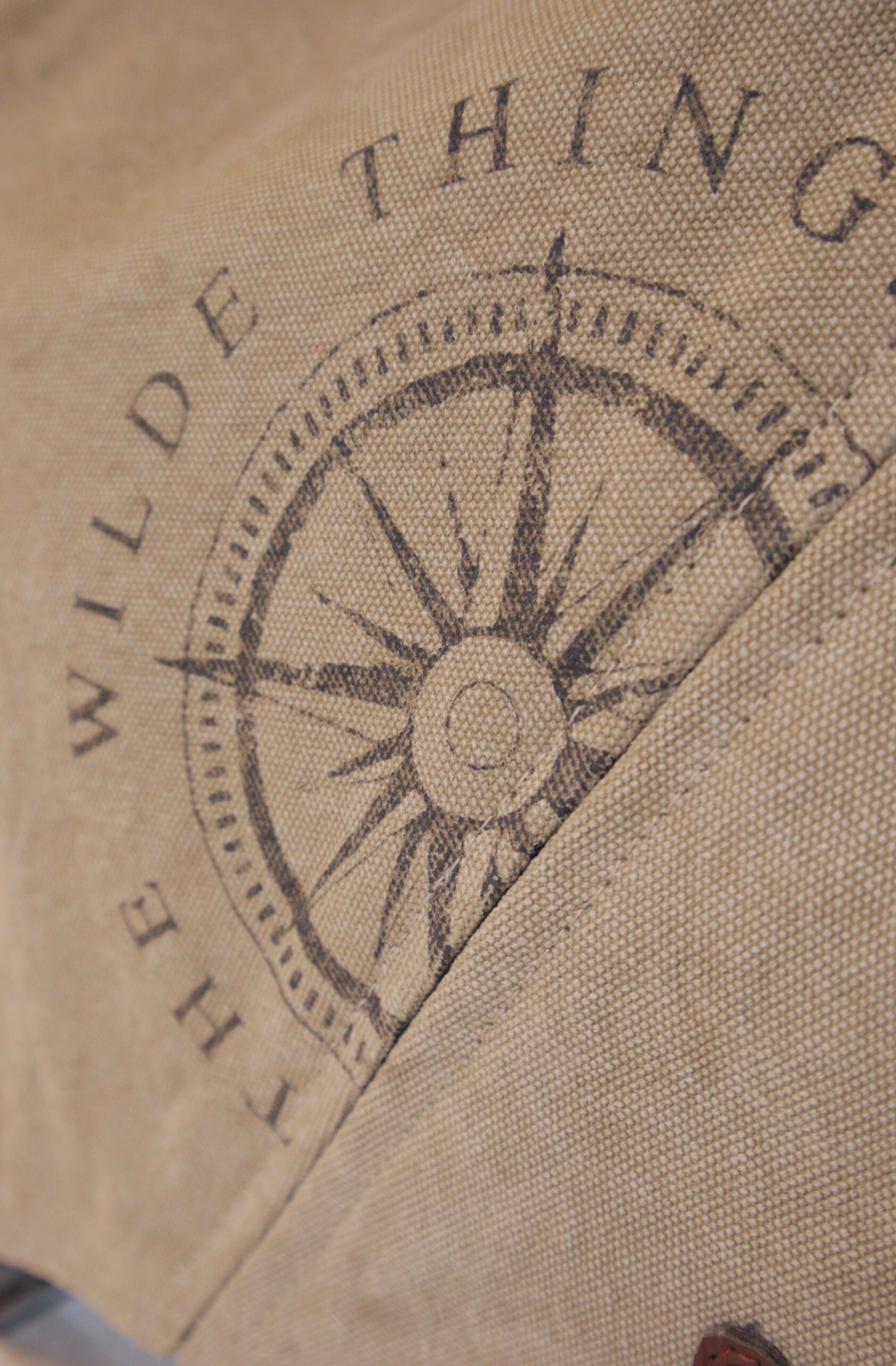 a closeup of the Where The Wilde Things are Compass logo stencilled on khaki coloured 100% cotton canvas