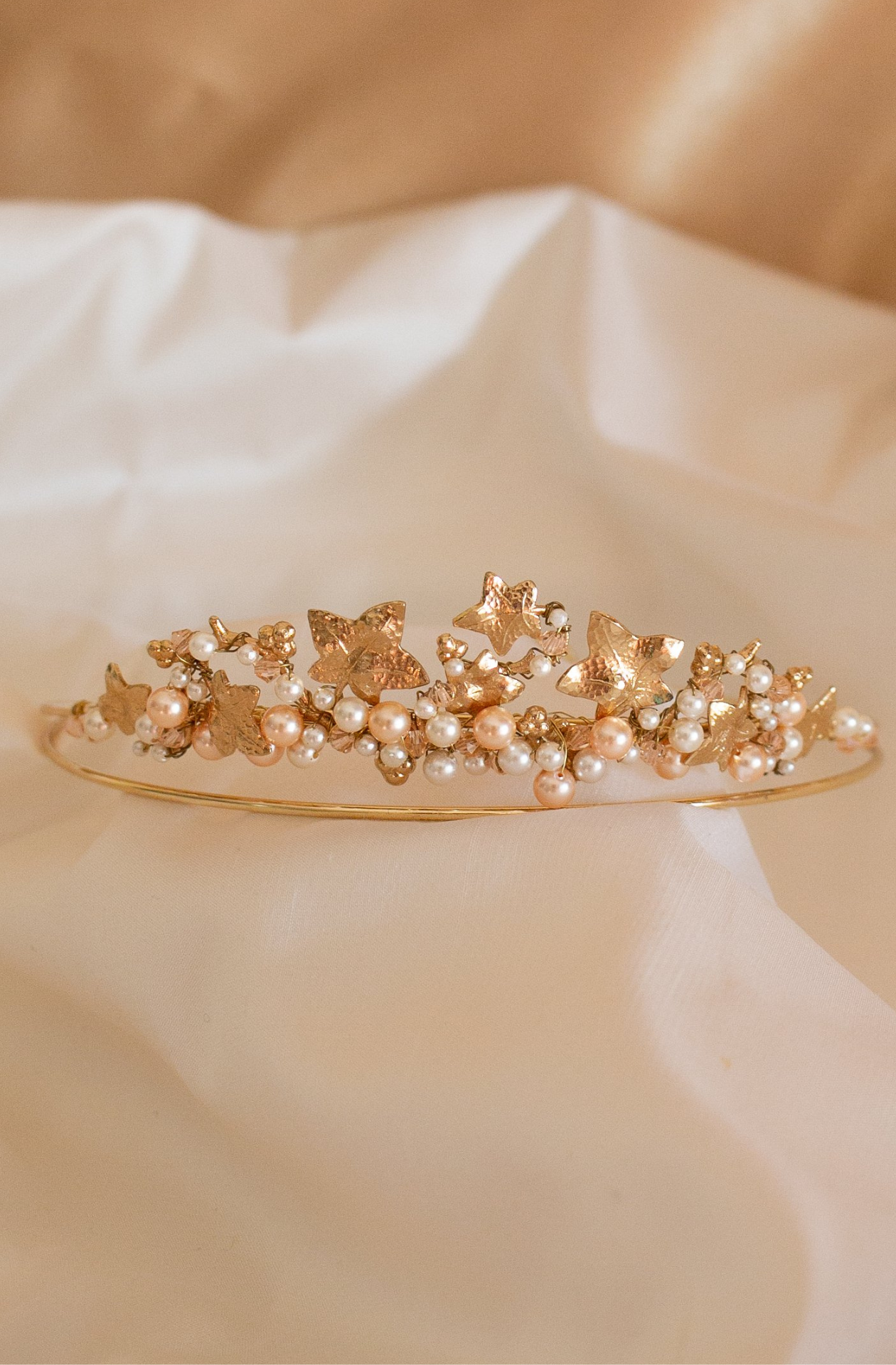 A handmade Swarovski white Pearl and Crystal Headpiece. A circular gold band holding the gems between a variety of floral and leaf metal shapes. A side angle shot