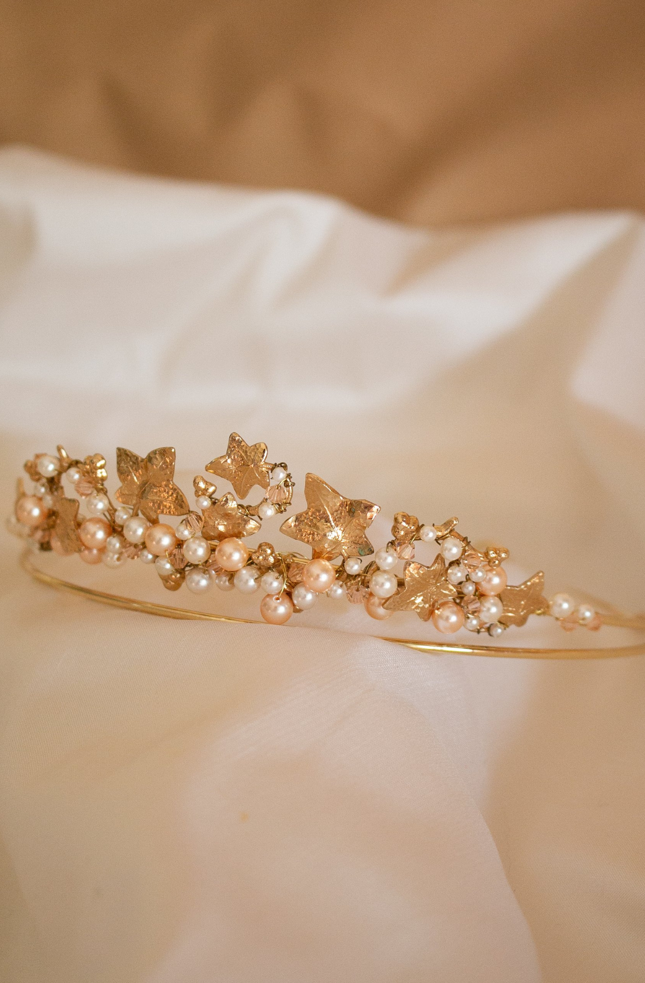 A close up of A handmade Swarovski white Pearl and Crystal Headpiece. A circular gold band holding the gems between a variety of floral and leaf metal shapes