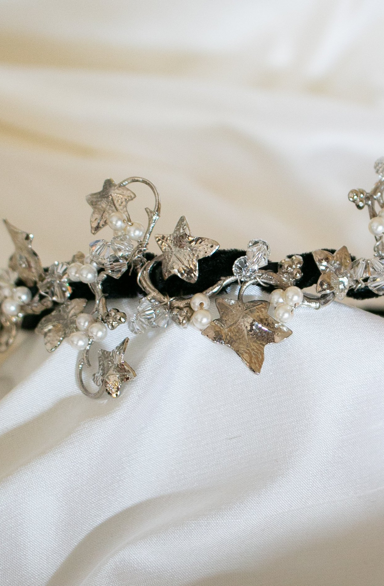 A Close up of A black headband with vine styles silver leaves sat atop the band, mixed in with swarovski pearls and crystals to create a beautiful arrangement