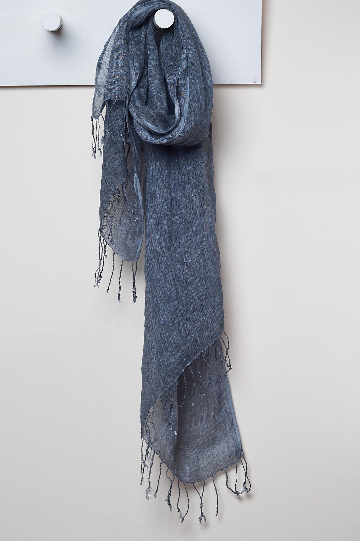 3 Visits To Cairo pure linen scarf in Graphite. looped around a hook detailing the linen texture and thin tassels tied at the short edges of the scarf.