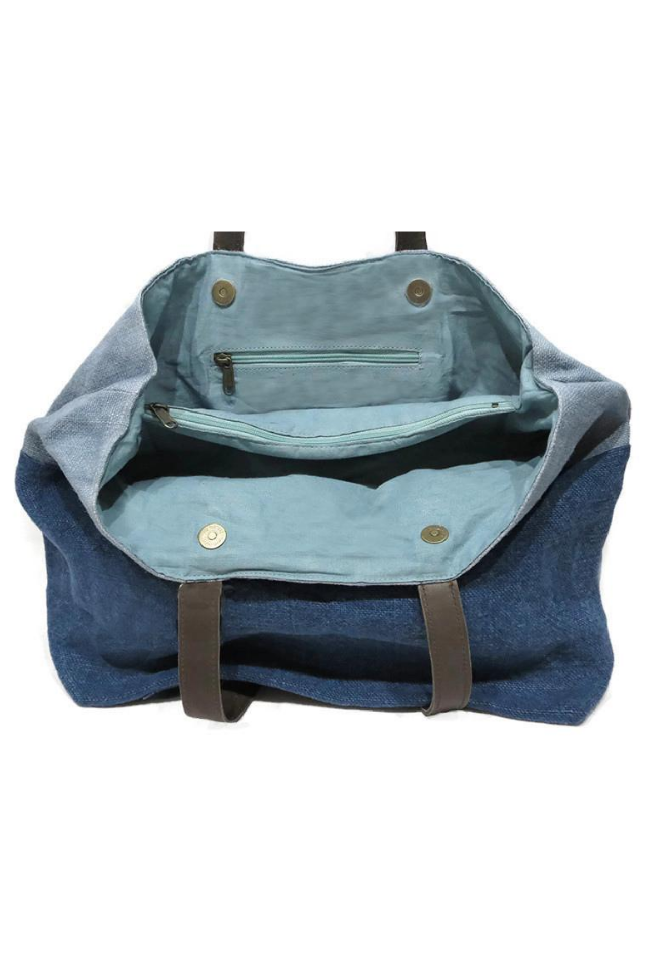 The thick light blue cotton lining of the double denim jute shoulder bag. The inside is split into three sections, two open sections either side of a large zip pocket. four metal clasps sit where the straps connect to the bag to keep the bag secure and closed.