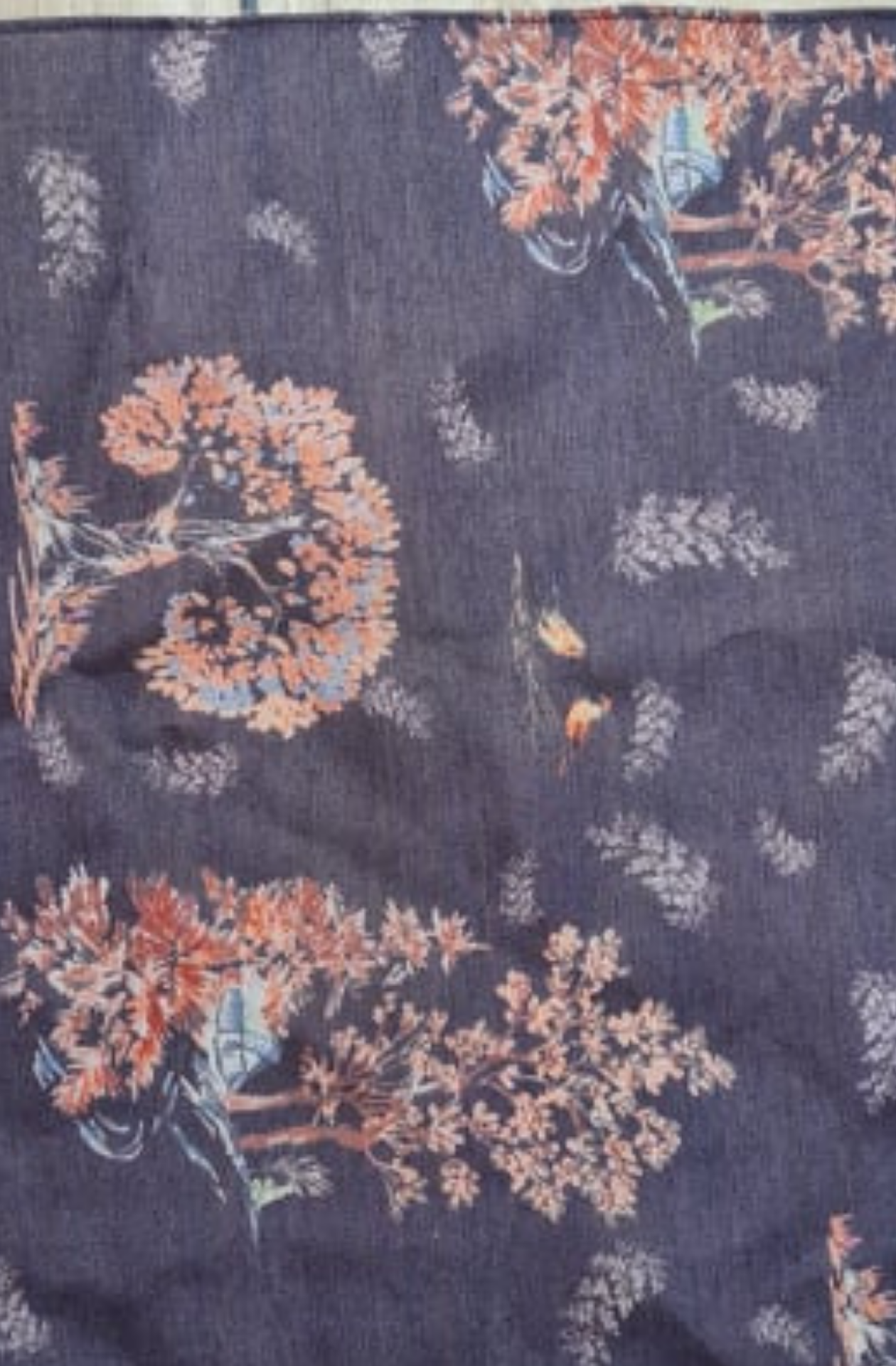 a deep blue silk pocket square featuring light blue and shades of orange trees, and light blue leaves dotted across the square