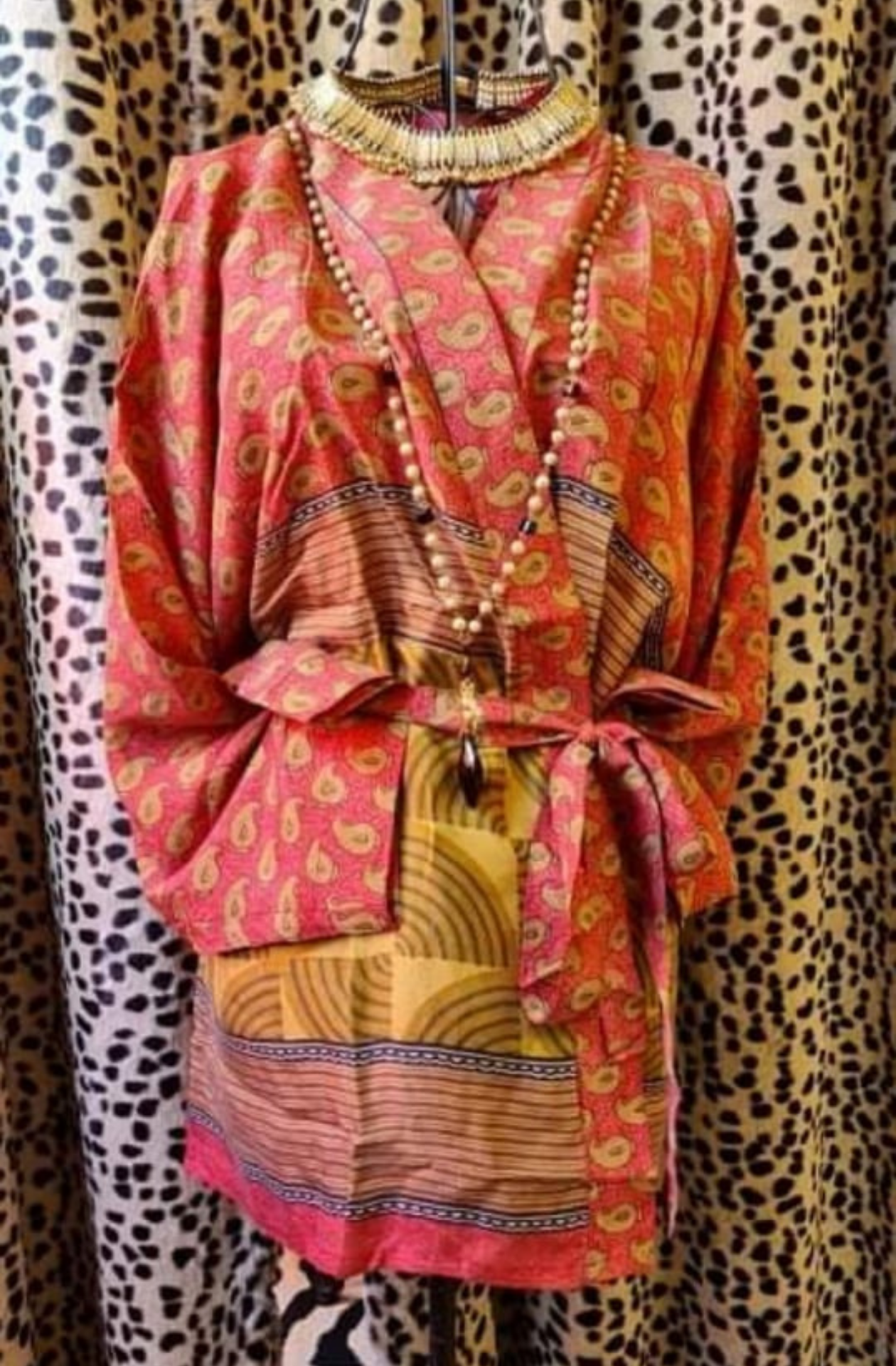 vintage sari silk kimono jacket displayed on a wire mannequin. The jacket is mostly and orange/salmon colour with a paisley yellow print. The bottom, half of the jacket appears more like a traditional japanese print with a variety of different line patterns and geometric circles in yellow and blue