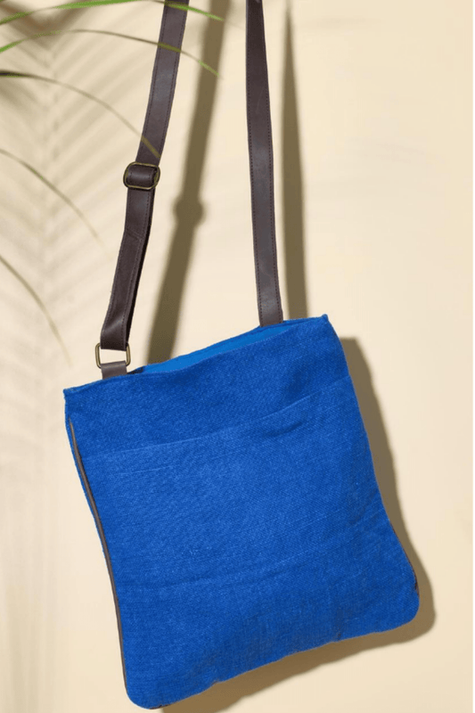 The "Cobalt" variant of the Hold Me Close Cross Body Bag. It is a vivid blue with an open front pocket and a black boning around the outside. An adjustable dark brown strap is connected on either side of the bag.