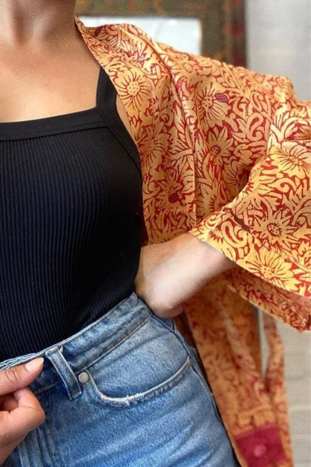 A close up on the kimonos shape showing wide sleeves and a relaxed boxy fit. The jacket has the same deep red colour, a bold floral pattern in a muted yellow tone.