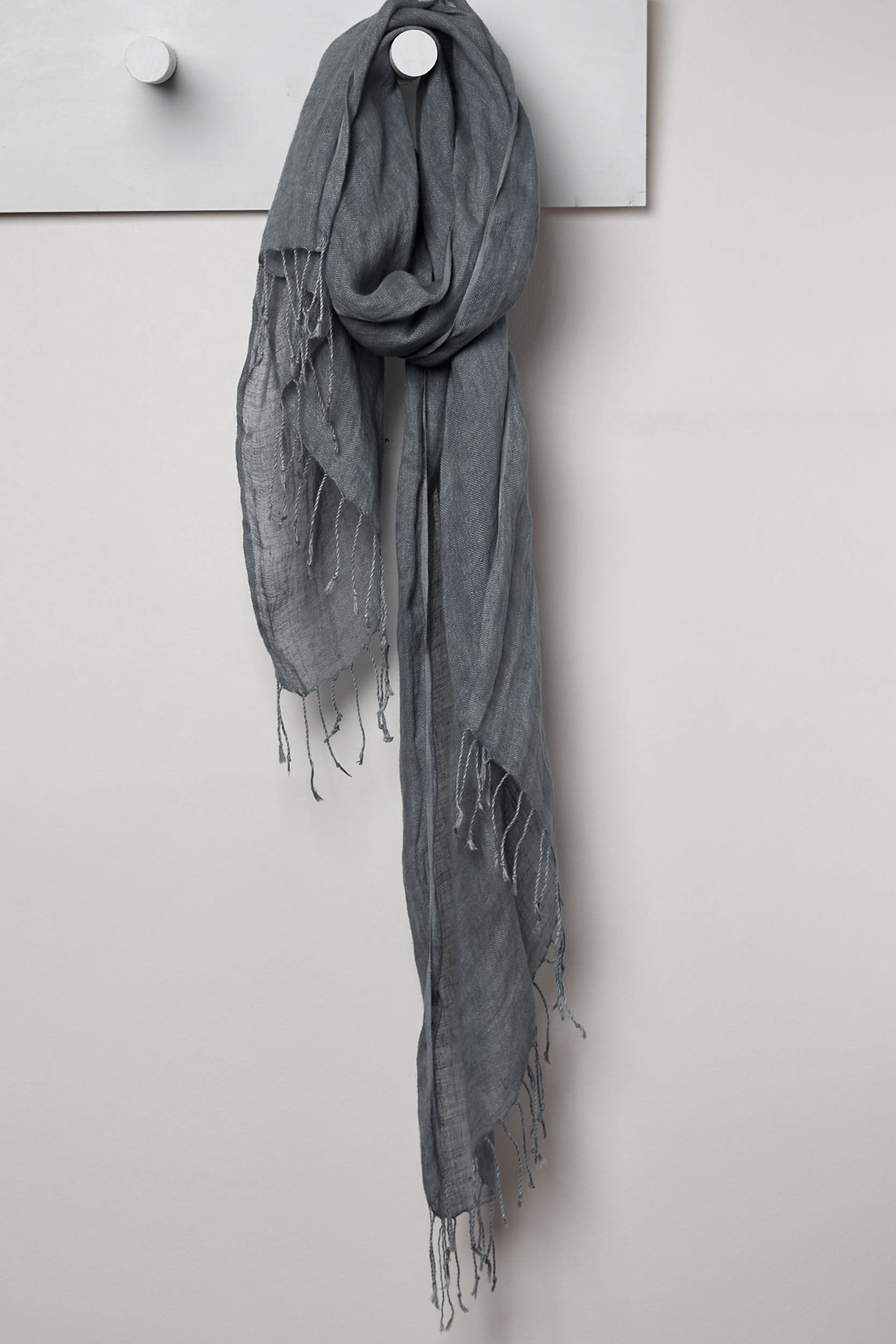 3 Visits To Cairo pure linen scarf in Storm. looped around a hook detailing the linen texture and thin tassels tied at the short edges of the scarf.