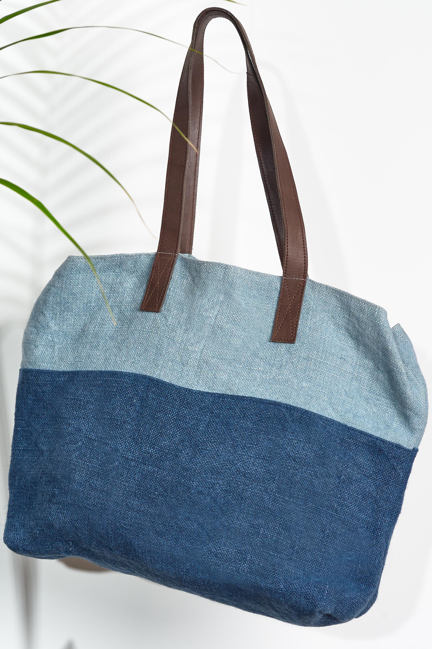 A large over the shoulder bag. With warm deep brown leather straps, and a two toned denim body. A light blue denim thick strip covers 1/4 of the bag and the rest is a classic deep blue denim.