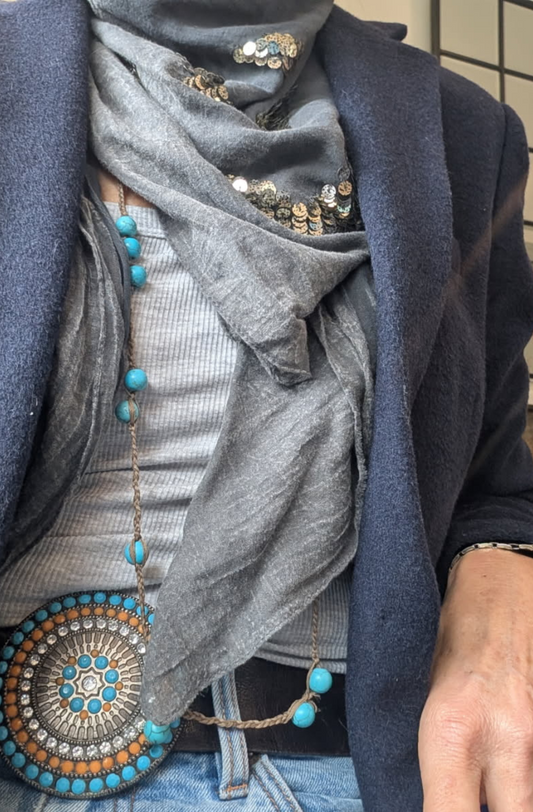 Person wearing a blue jacket with a grey cotton scarf embellished with sequins, wearing turquoise decorative elements.