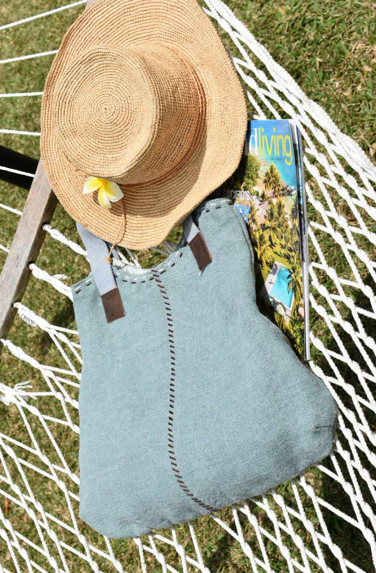A faded blue jute shoulder bag lies on a hammock with a stylish Panama hat, copy of Island Living magazine and fresh frangipani. Photo taken in Port Vila.