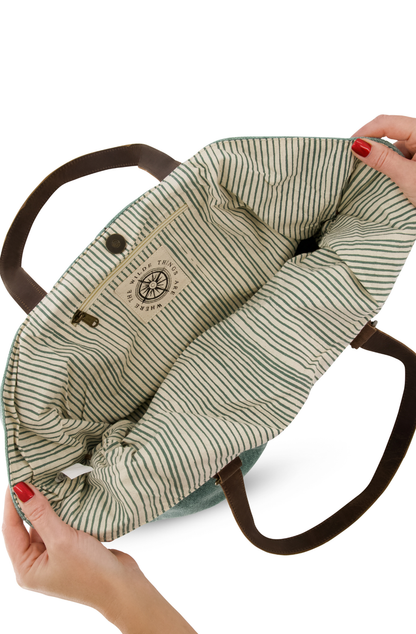 a model holds the top of a jute shouder bag open to show the pin striped cotton lining which is colour matched to the outer colour of the bag. also seen are the two leather shoulder straps.