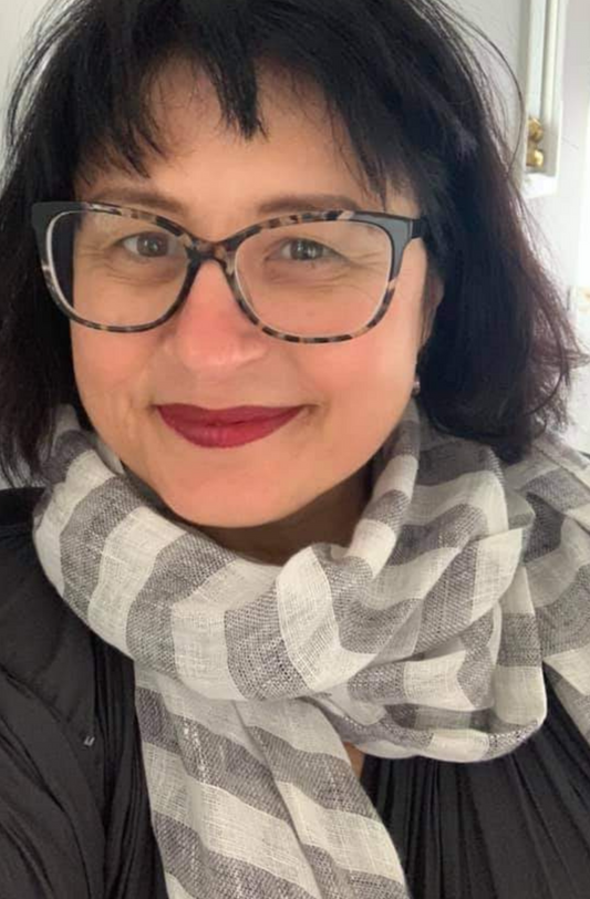 a smiling woman with a dark bobbed haircut wearing glasses and a striped linen scarf in a striped pattern of white and black/blue