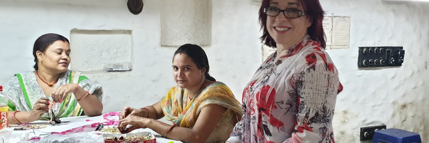 Ingrid chatting to 2 Indian women in traditional saris, workin on jewellery pieces in a women run studio in New Delhi