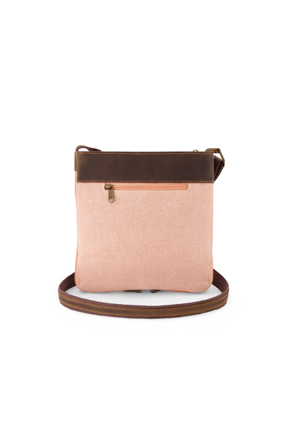 The reverse side of a peony pink jute mini crossbody bag showing a hidden zip pocket which would sit against the body when worn. Trim is a mid brown leather and a strap can be seen which is brown cotton webbing with a strip of leather stitched along the length of the strap.