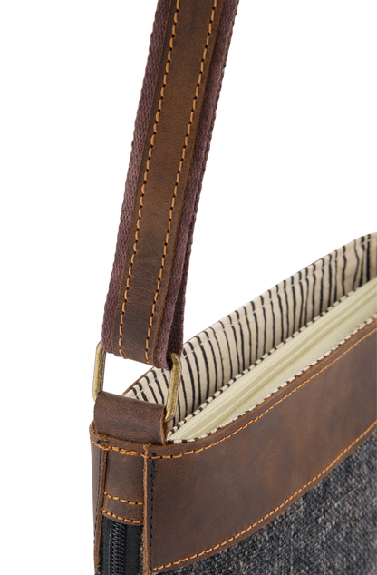 detail of rectangular brass link strap attachment to a mini crossbody bag in smoky black jute with leather trim,. bag is trimmed with mid brown leather, which also trims the length f the adjustable strap.