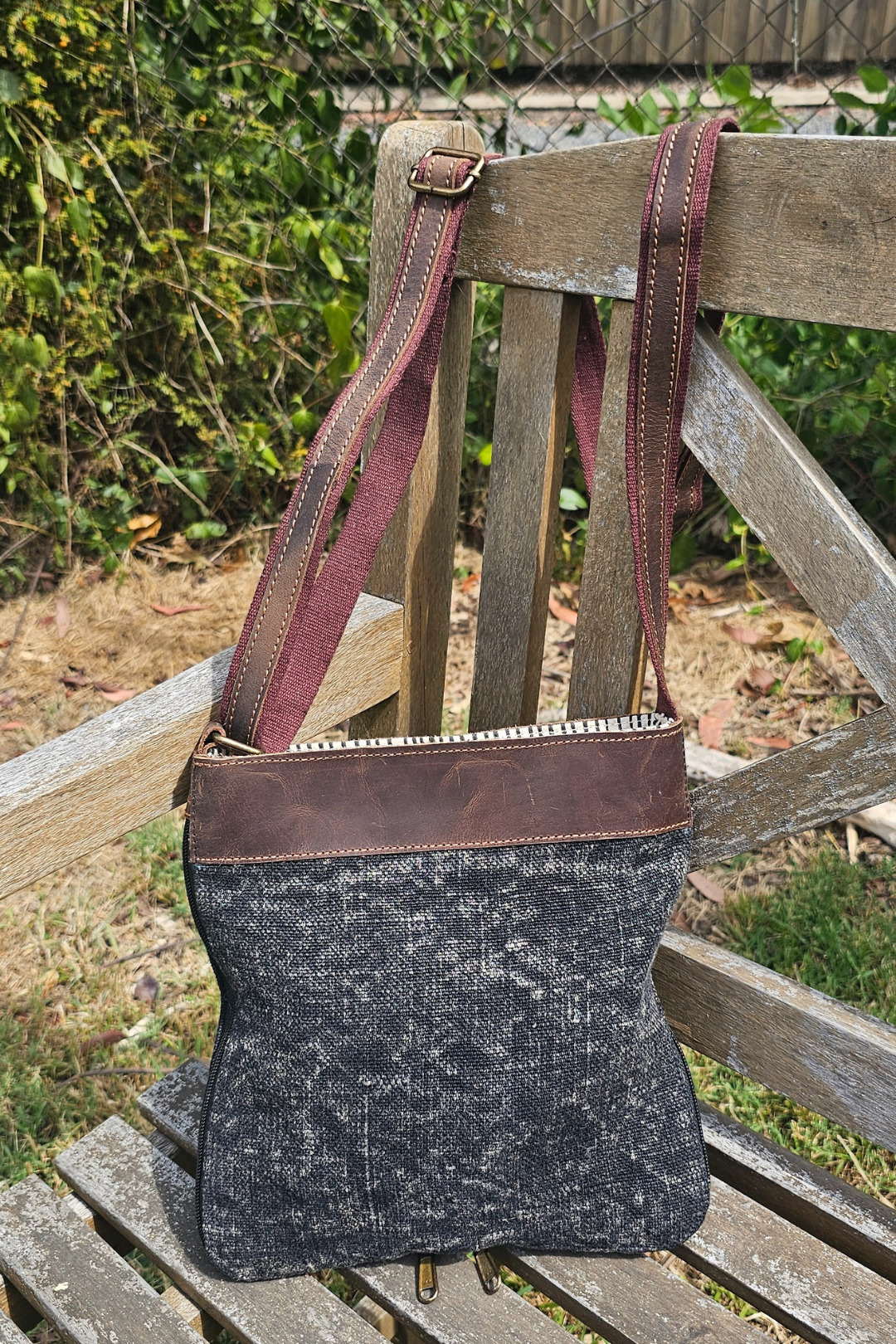 A Graphote coloured mini crossbody bag sits on a distressed wooden bench just showing a little of the striped cotton lining 