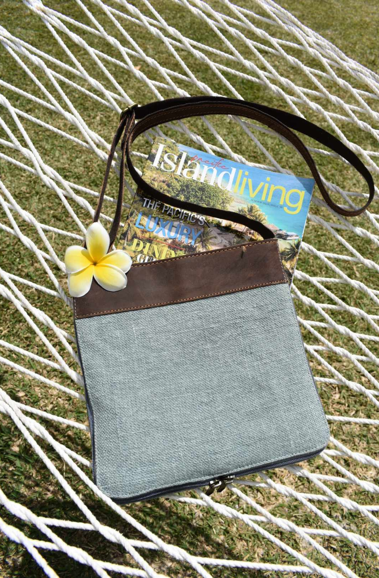 blue mini jute crossbody ag lying on a hammock in Port Vila with a fresh frangipani ontop of a copy of Island Living Magazine