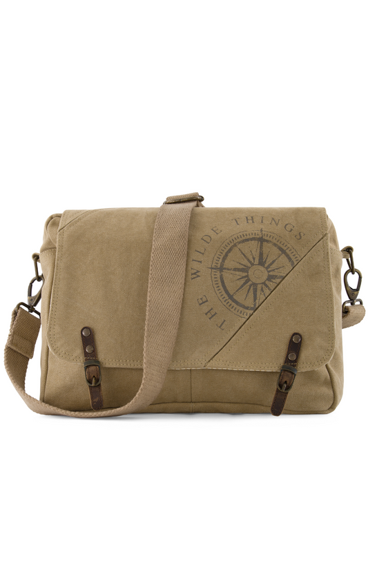 a canvas crossbody satchel with strap drapped over the front, showing compass logo screen printed on the front, leather tabs, and brass hardware attaching the adjustable strap to the sides of the satchel