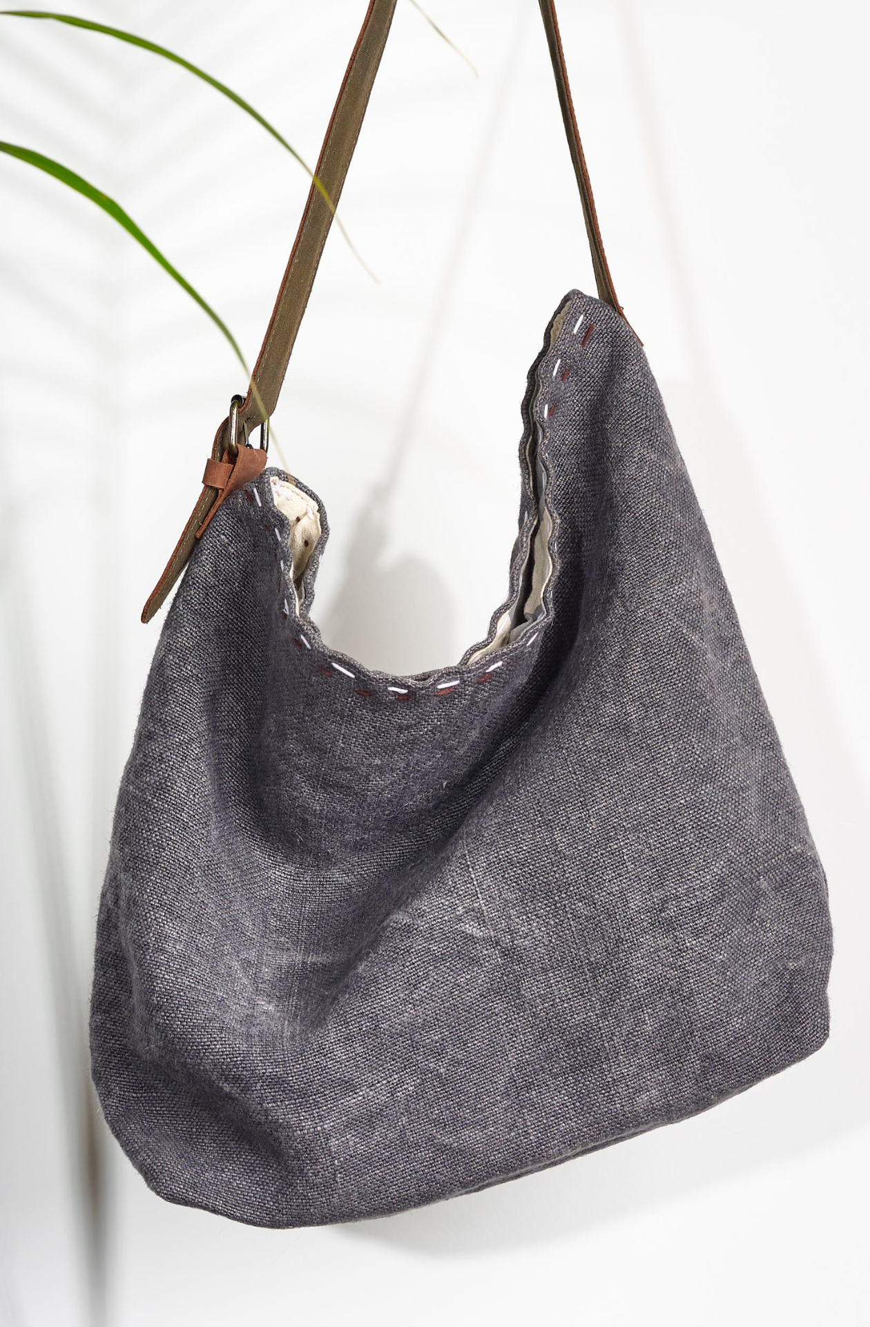 Charcoal All the world Jute Bag. The washed dark grey is contrasted with two lines of black and white stitching at the top of the bag in between the warm brown leather strap with a golden buckle. 