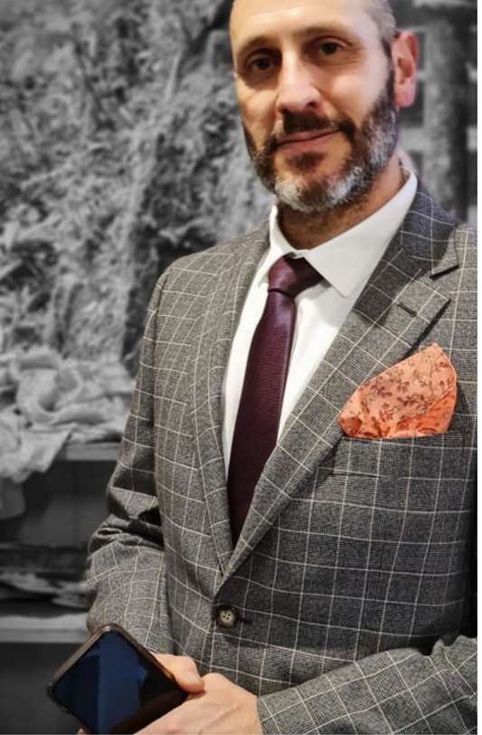 an orange floral patterned pocket square sitting in the pocket of a man in a grey suit with matching tie