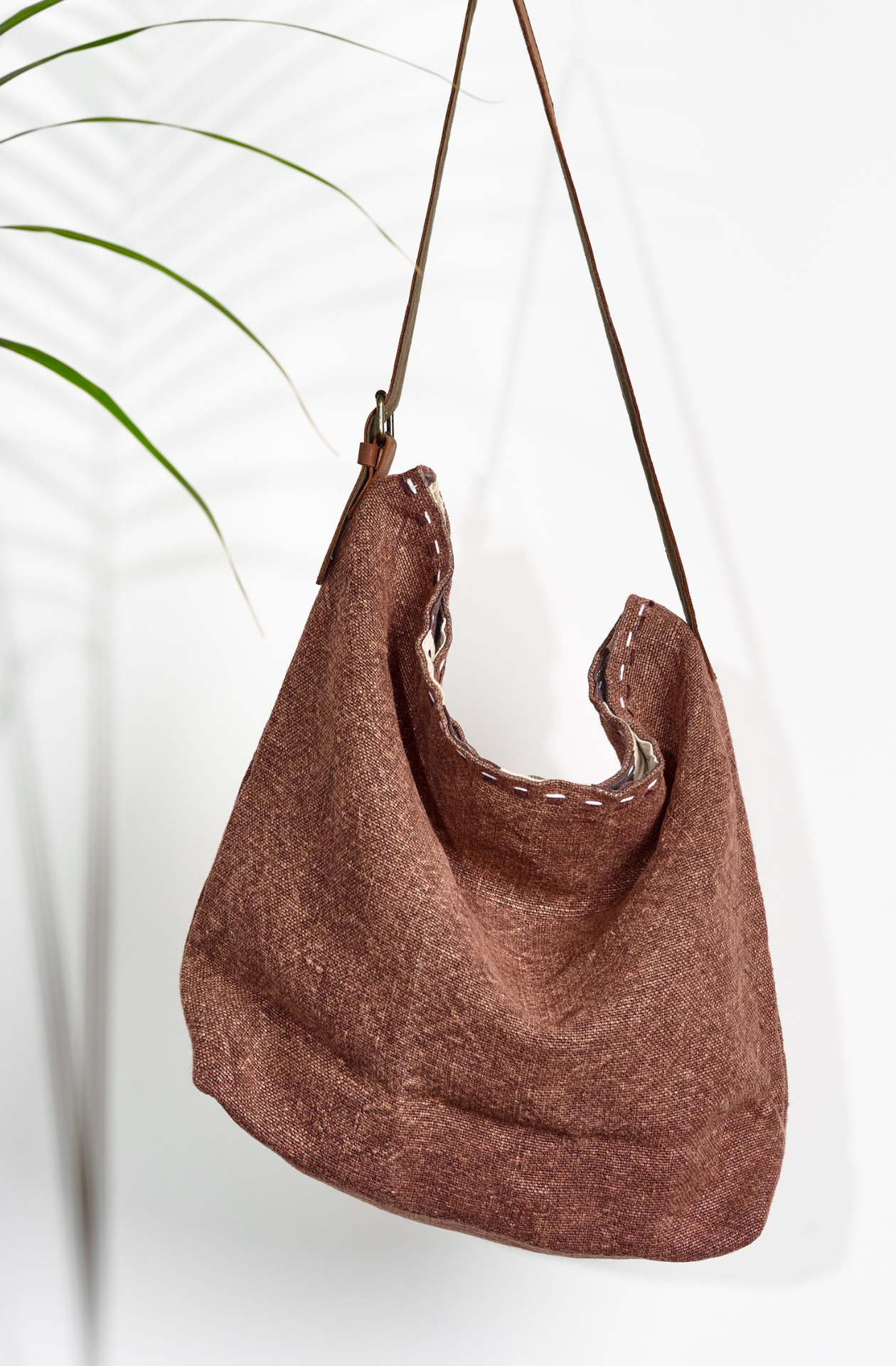 Mocha All the world Jute Bag. The washed warm medium brown is contrasted with two lines of black and white stitching at the top of the bag in between the warm brown leather strap with a golden buckle. 