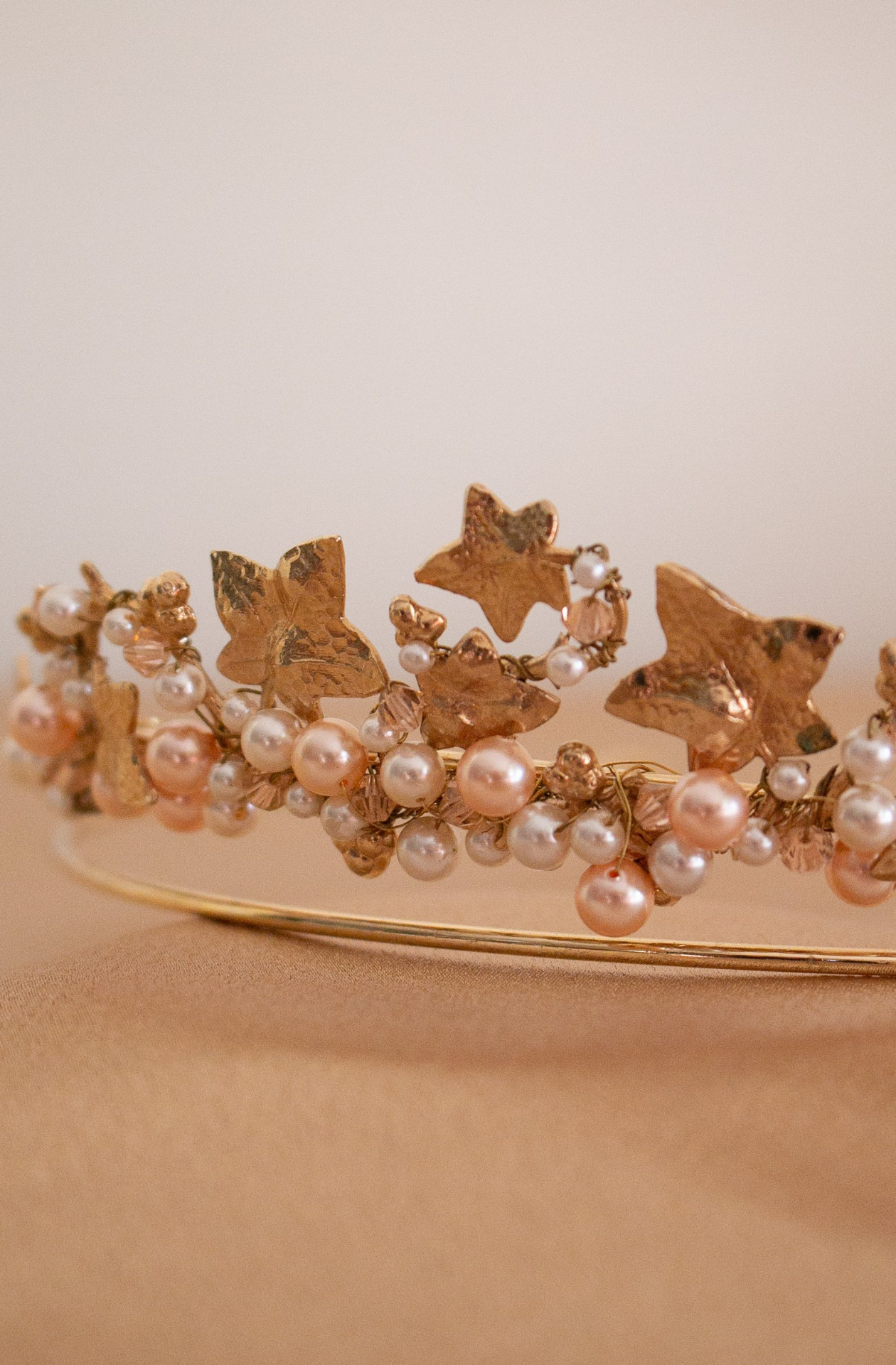 A close up of A handmade Swarovski white Pearl and Crystal Headpiece. A circular gold band holding the gems between a variety of floral and leaf metal shapes