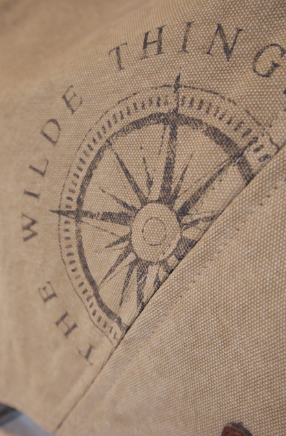 a closeup of the Where The Wilde Things are Compass logo stencilled on  khaki coloured 100% cotton canvas 