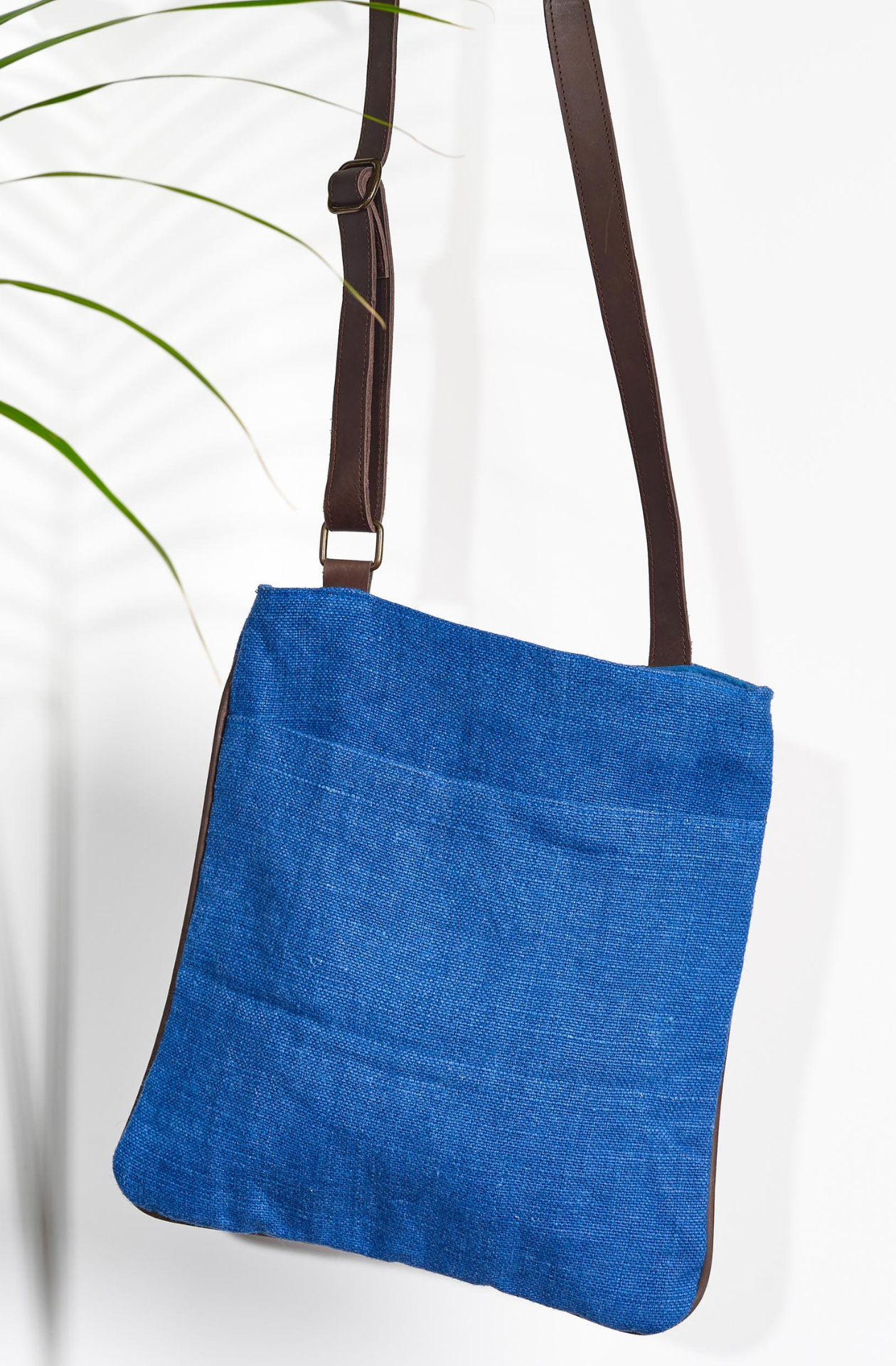 The "Cobalt" variant of the Hold Me Close Cross Body Bag. It is a vivid blue with an open front pocket with matching piped leather around the outside. An adjustable dark brown strap is connected on either side of the bag.