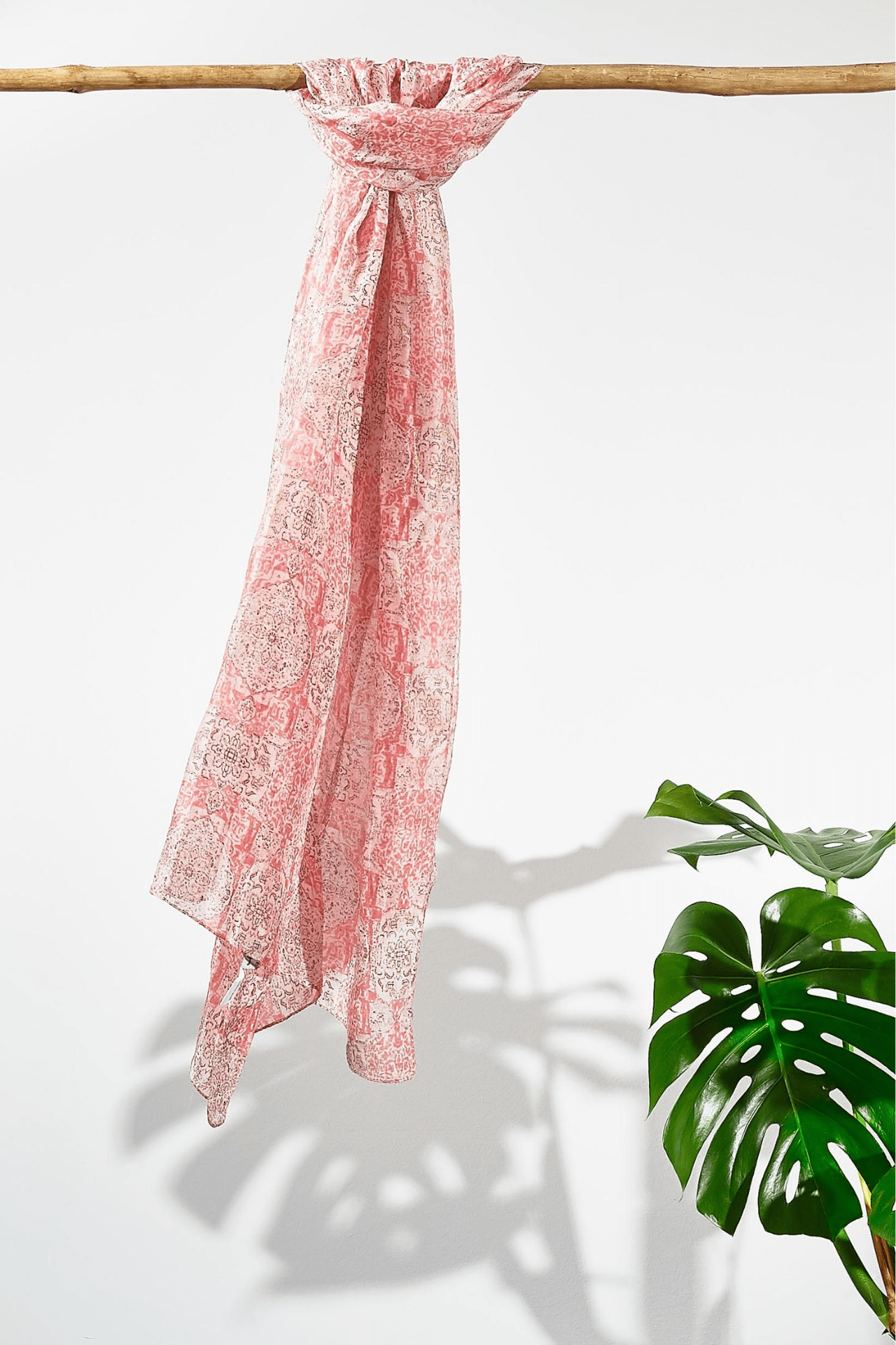 The rosewater moroccan silk scarf hanging from a rod. Showing how smooth the silk is as it hangs. The scarf is a light pink with a dark pink busy pattern on it