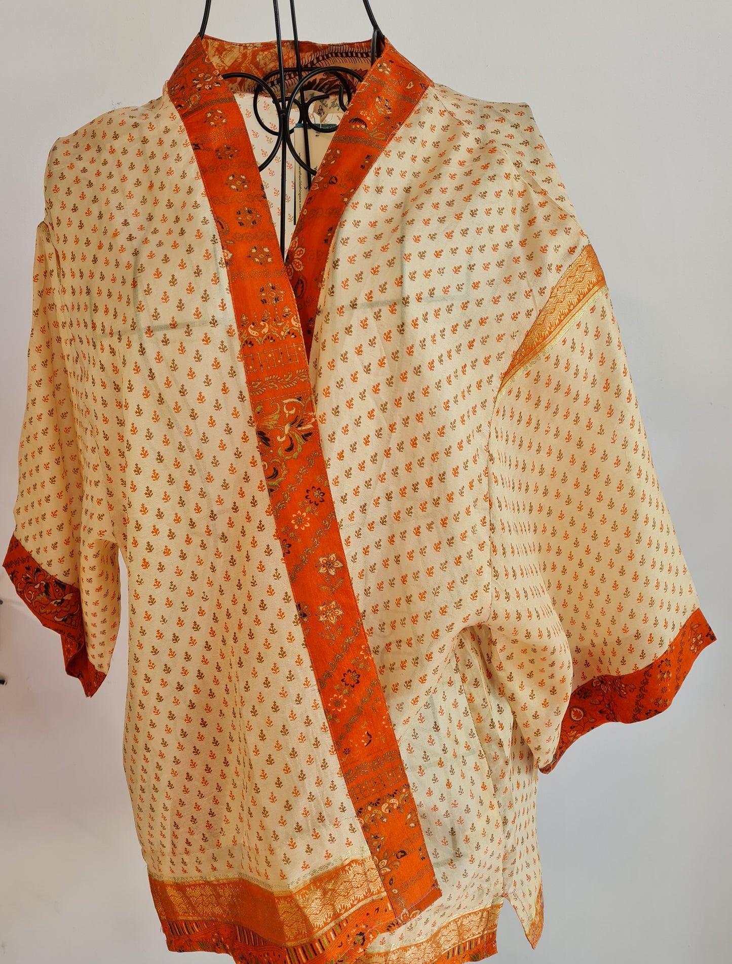 Mandarin Palace a very pale yellow muse jacket crossed over a wire mannequin. it features a very simple orange and brown leaf pattern cover the whole thing. a deep vibrant orange trims every edge of the jacket with black and gold accents.