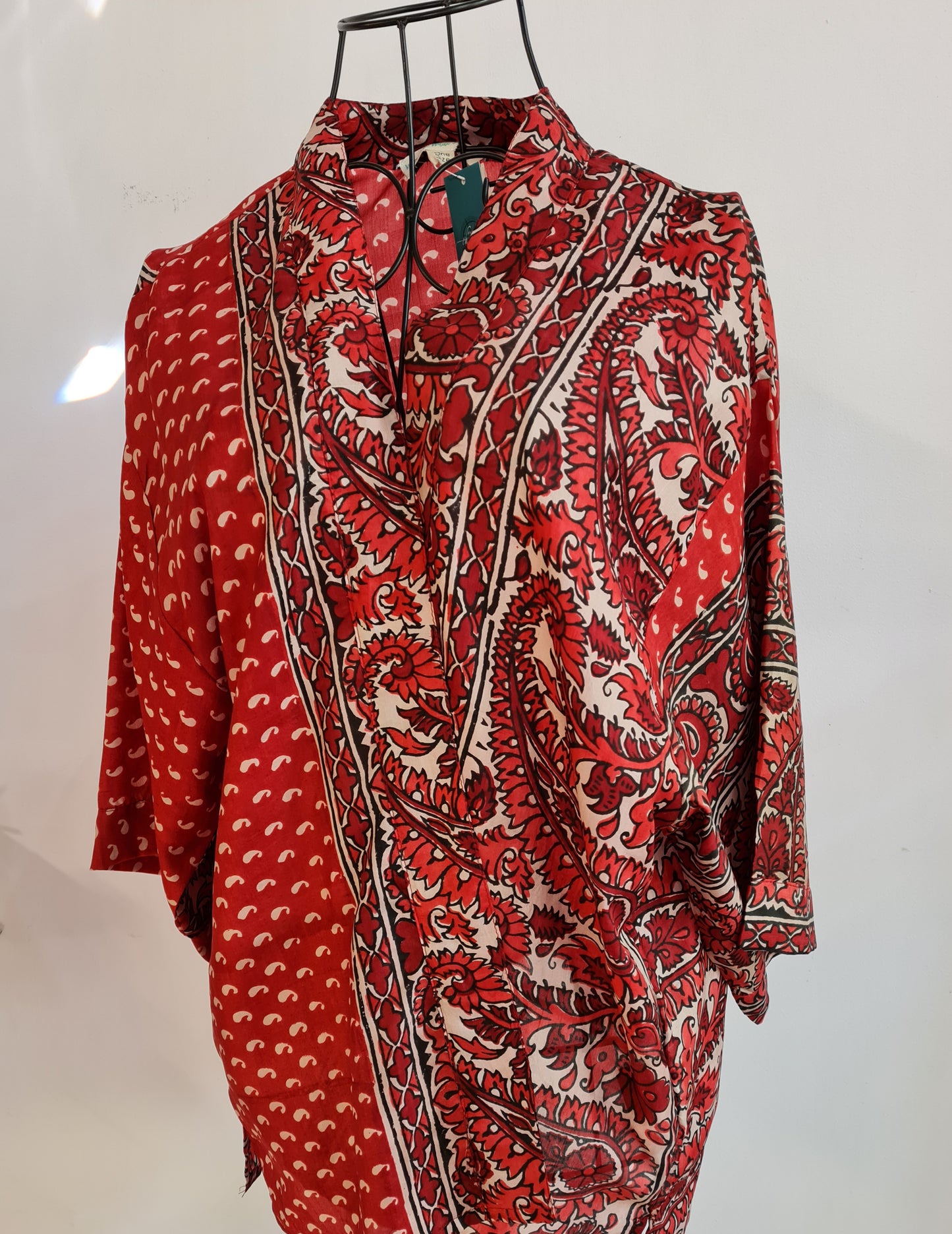 a red and white muse jacket crossed over a wire mannequin. 1/4 of the jacket is a deep red with small asymmetrical white dots evenly spaced across the surface. The other 3/4s is a large proportioned paisley pattern in shades of red against a white background. 