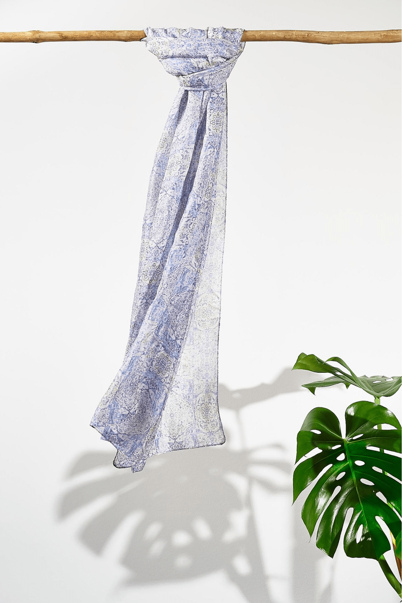 The blue mist moroccan silk scarf hanging from a rod. Showing how smooth the silk is as it hangs. The scarf is a pale sky blue with a dark blue busy pattern on it