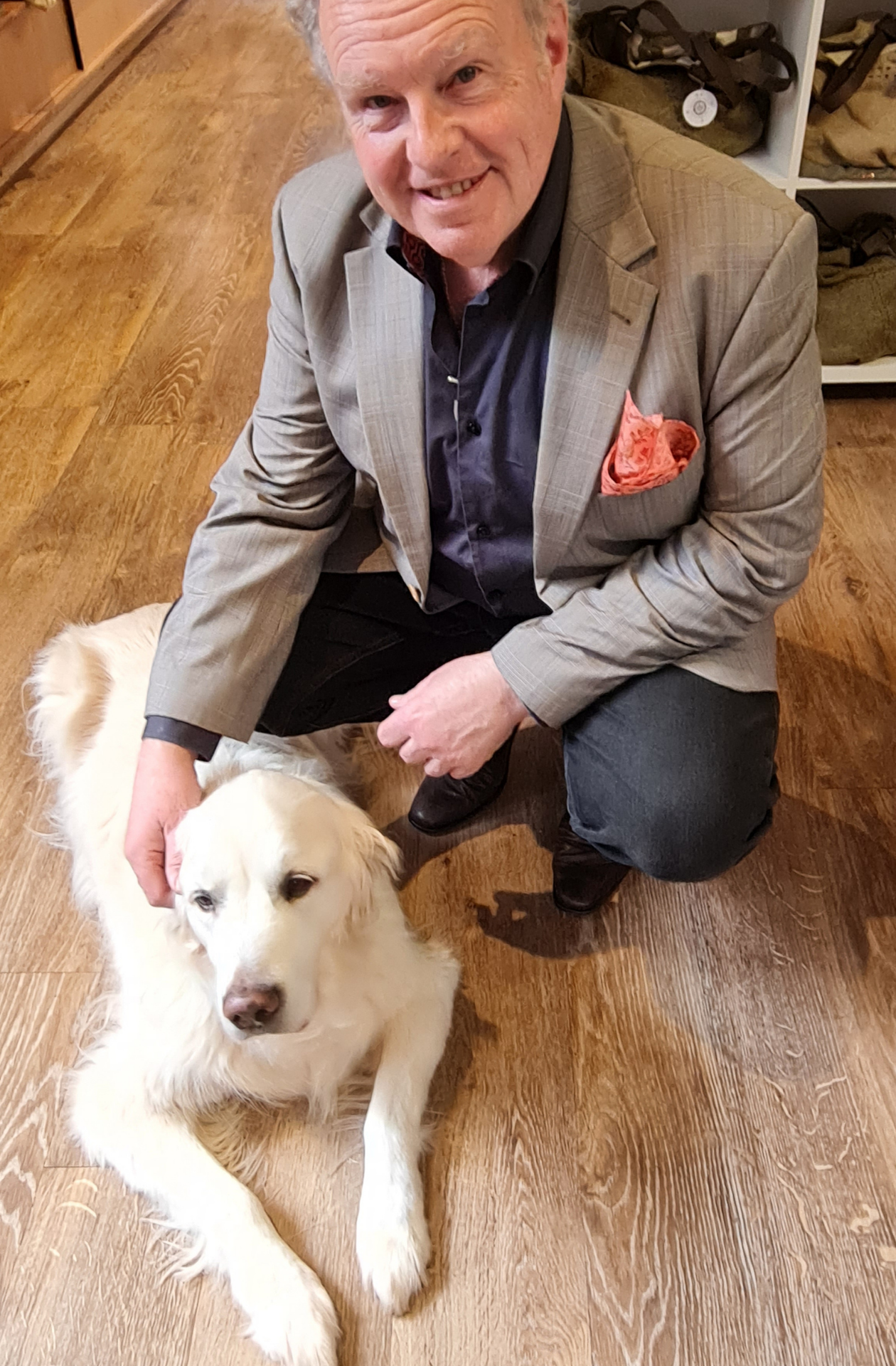 Portrait of a man with an orange flore silk pocket square in the pocket of a grey suit. The man is patting a golden retreiver