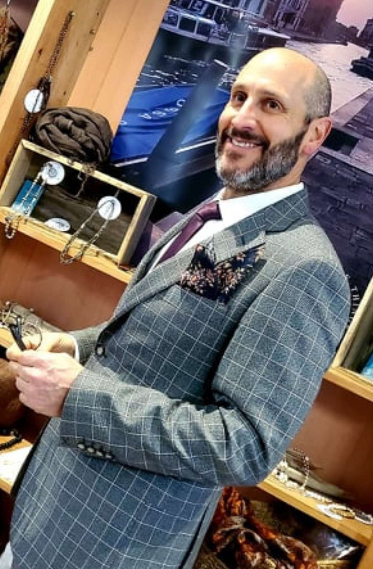 A portrait of a man in a grey checkered suit with a black pocket square featuring a striking floral pattern