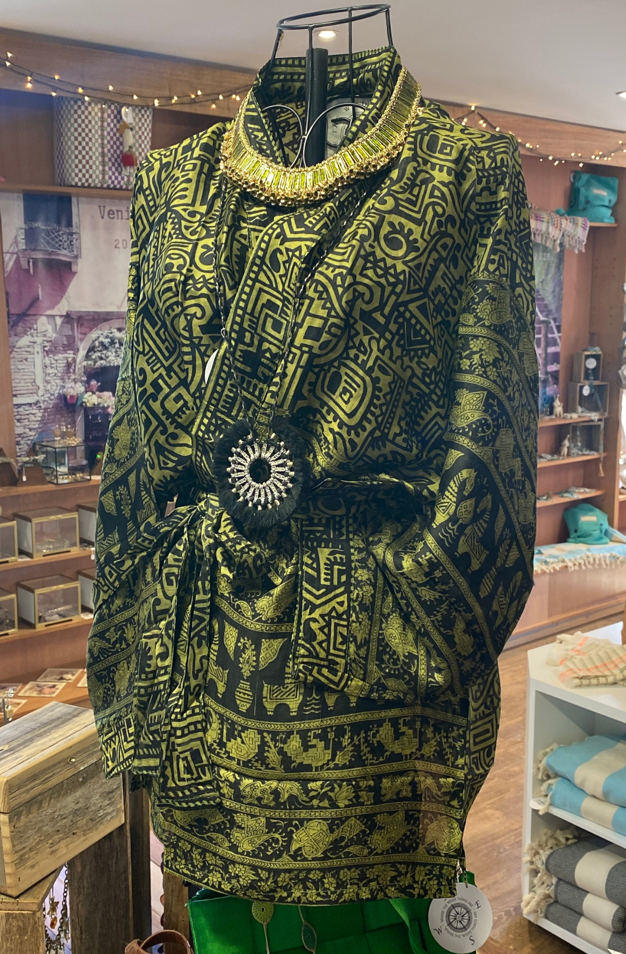 A vintage sari silk kimono jacket displayed on a wire mannican. The jacket is a deep lime green with a black block print of various busy swirls, geometric patterns, creatures and many other things.