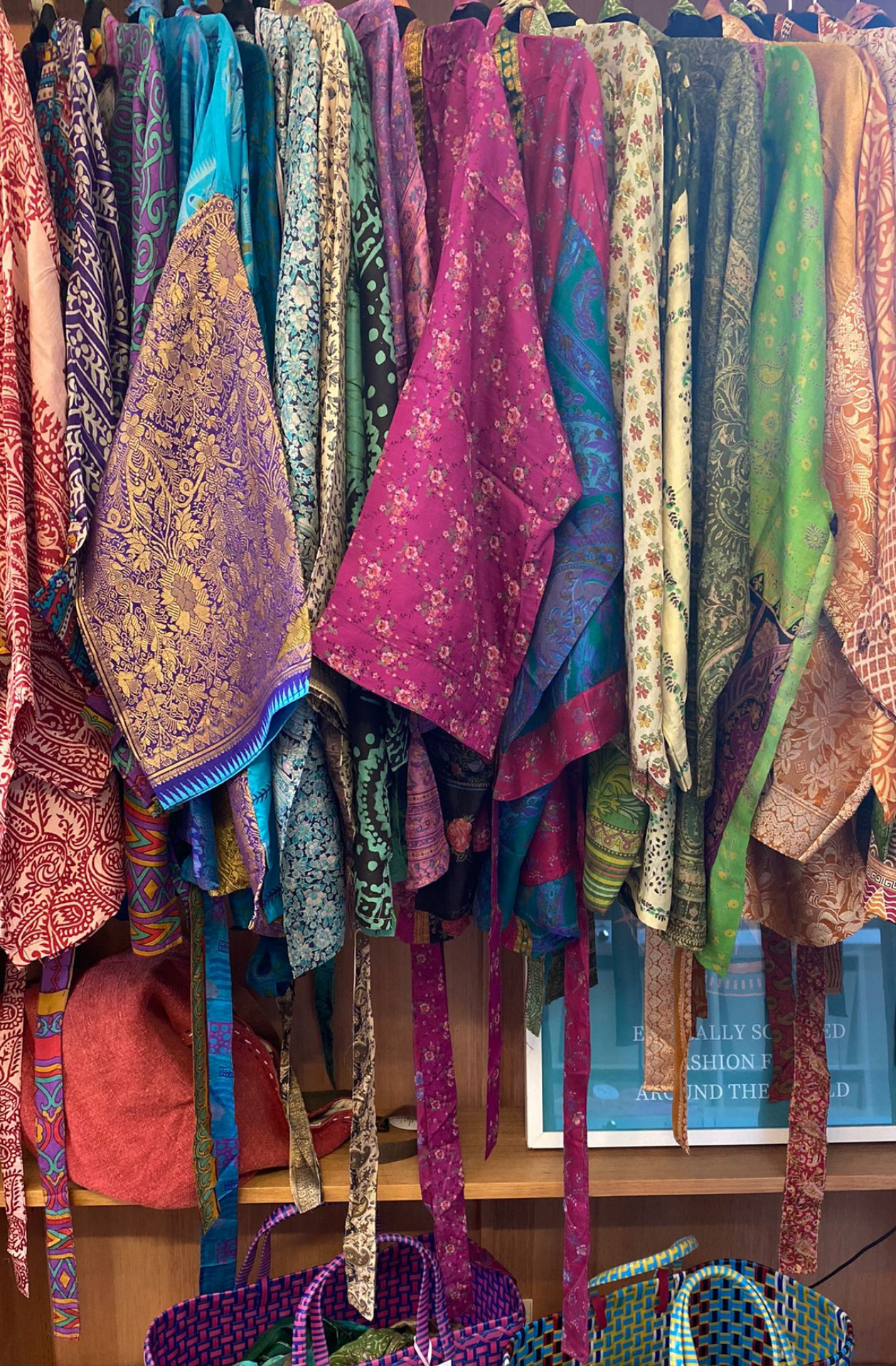 A collection of sari silk jackets lined up next to eachother to show how many colour varieties there are.