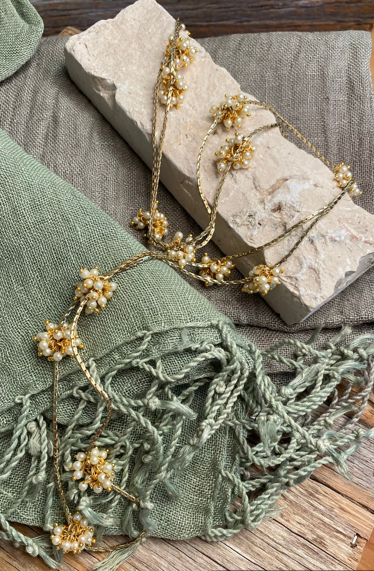 sage green and jungle moss linen scarves sit on a table with a necklace draped over top. The close up shot shows the twisted tassel details on the end of each scarf.