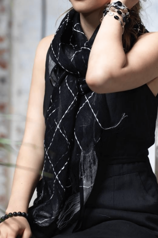A portrait of a woman wearing a black and white coastal linen scarf. The scarf linen is black and the detail white stitching is in a criss cross pattern across the whole scarf. 