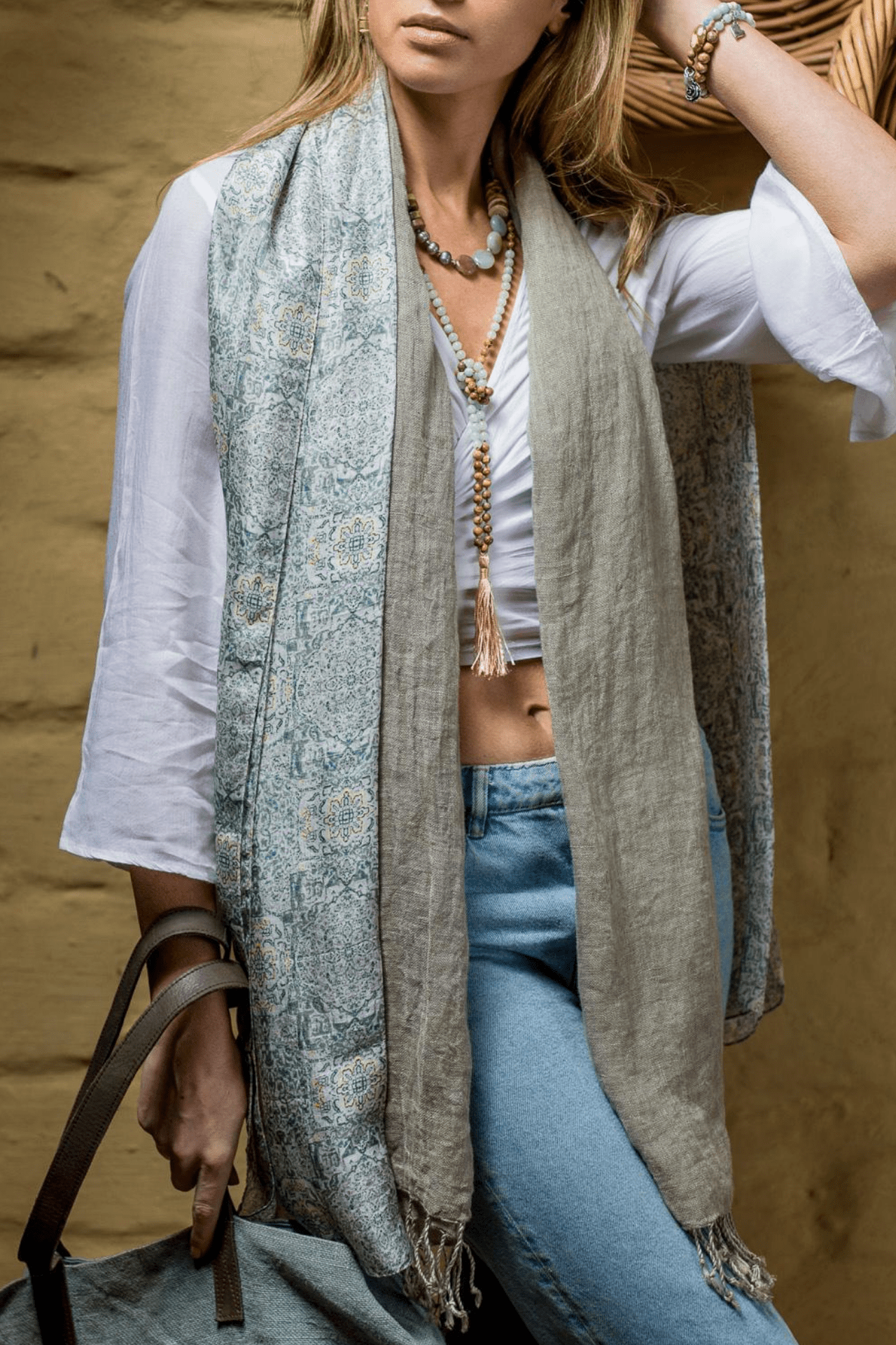 A woman styles the blue mist arabesque moroccan silk scarf around her neck beside a mild grey linen scarf and a blue toned outfit.