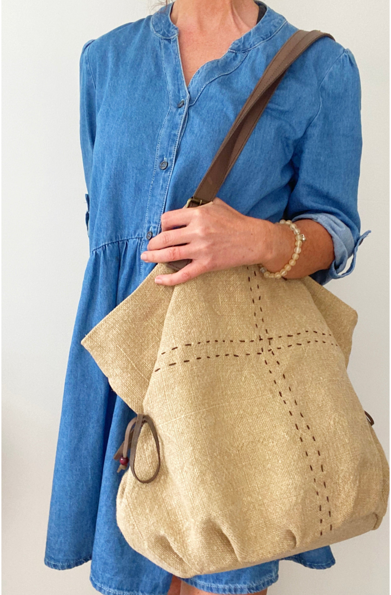 A woman in blue denim with a jute slouch bag over her shoulder in the colour biscotti