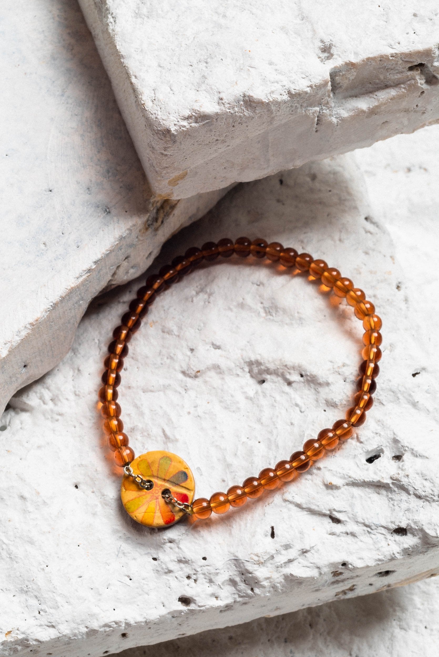 a semi-opaque warm honey brown beaded coconut bracelet with a coconut shell charm with a subtle rainbow flower in a water colour style